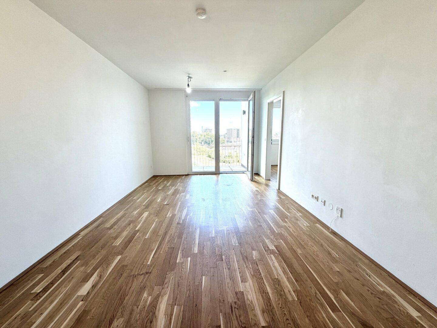 Lichtdurchfluteter Wohnraum mit Parkettboden und Zugang zu einem Balkon.