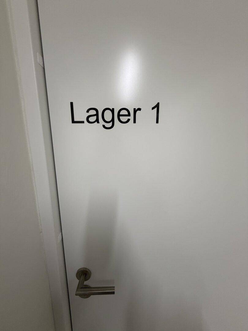 Weiße Tür mit der Aufschrift "Lager 1" und einem einfachen Türgriff.
