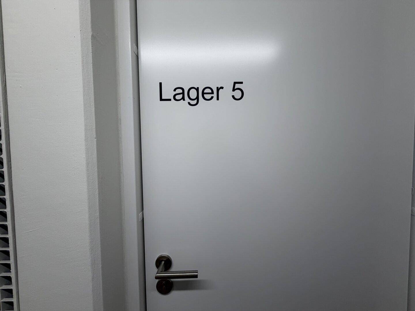 Weiße Tür mit der Aufschrift "Lager 5" und einem schlichten Türgriff.