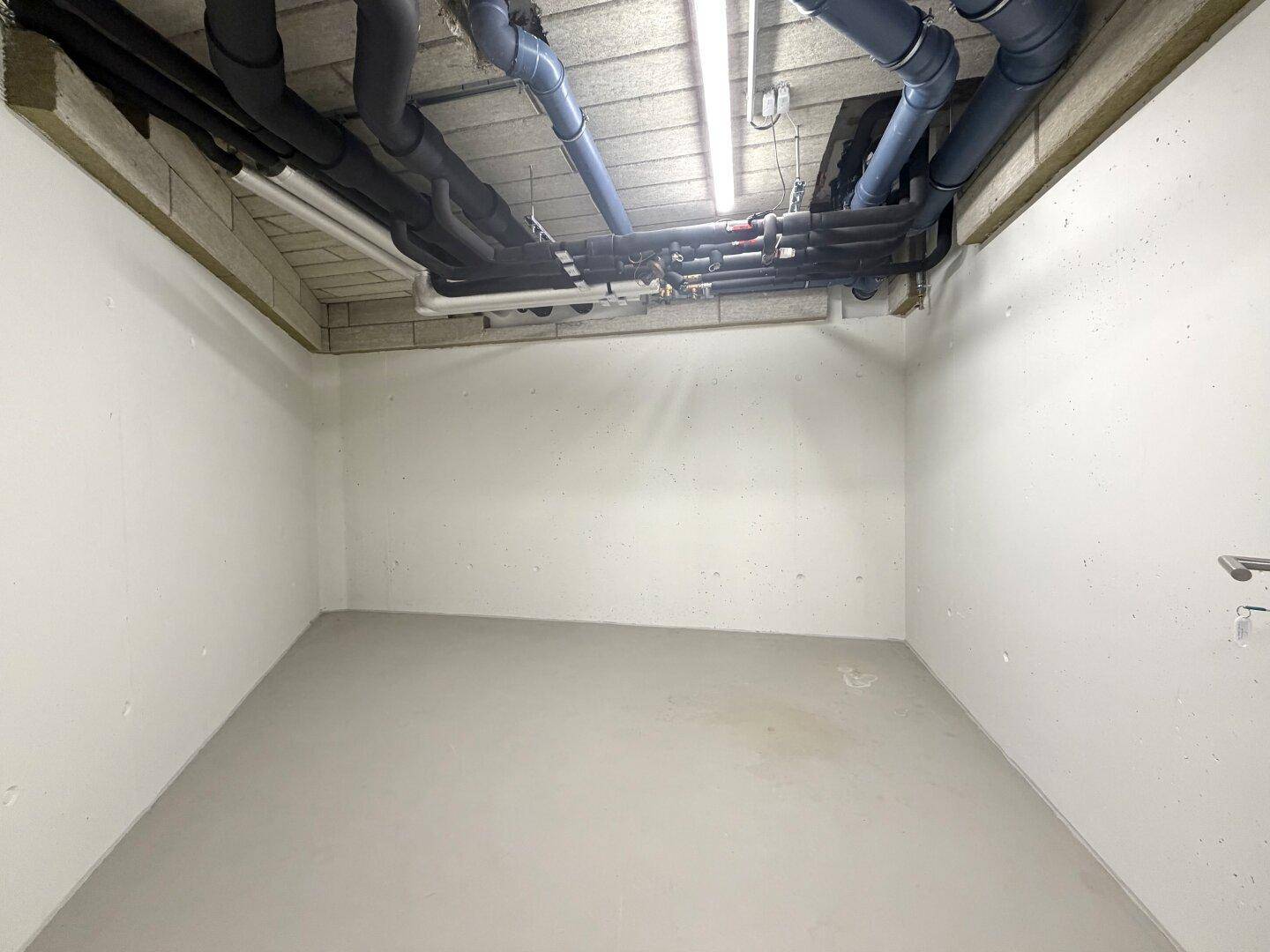 Leerer Lagerraum mit vielen sichtbaren Rohren und Leitungen an der Decke.