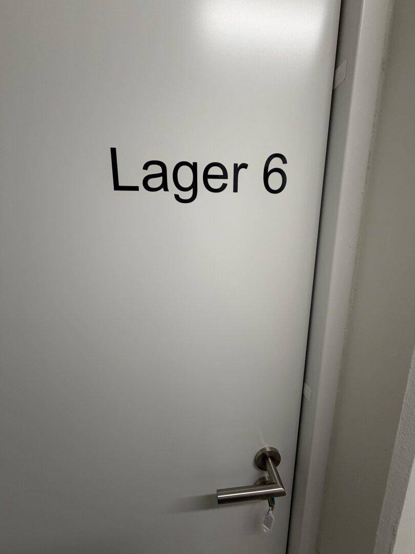 Weiße Tür mit der Aufschrift "Lager 6" und einem modernen Türgriff.