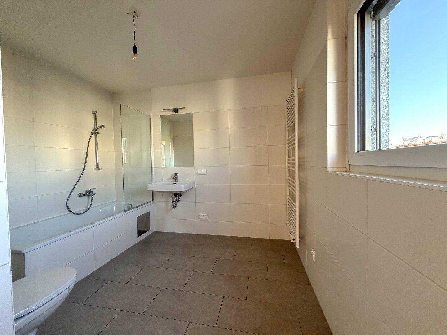 Modernes Badezimmer mit Badewanne, Dusche, Fenster und beheiztem Handtuchhalter.