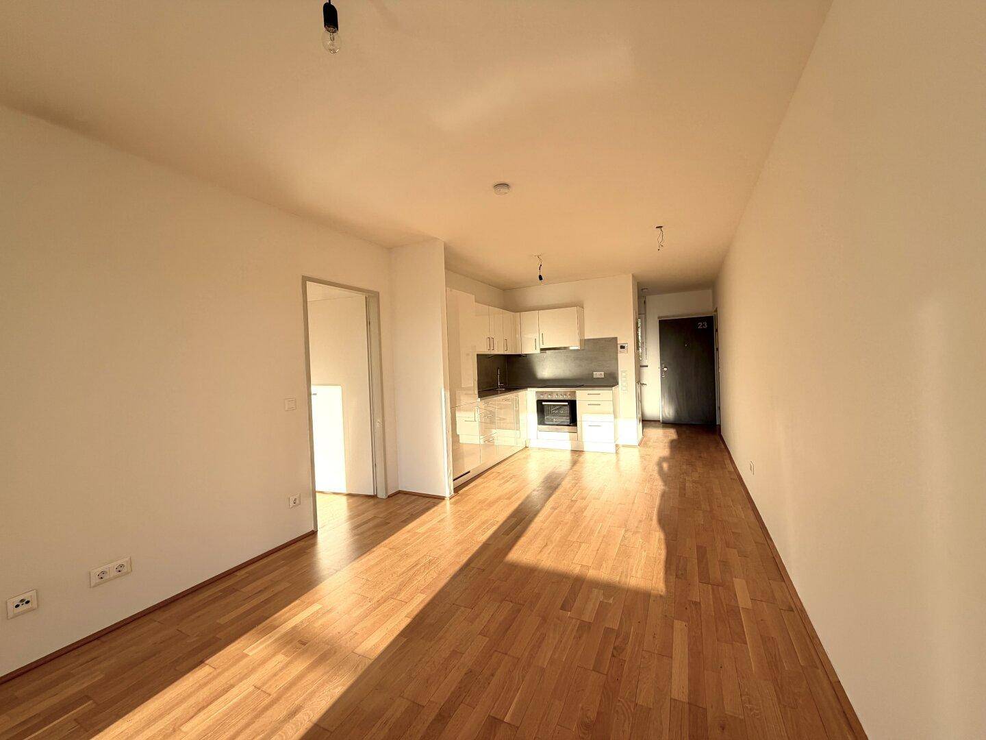 Geräumiger Wohnbereich mit Holzboden und moderner Küchenzeile in hellem Design.