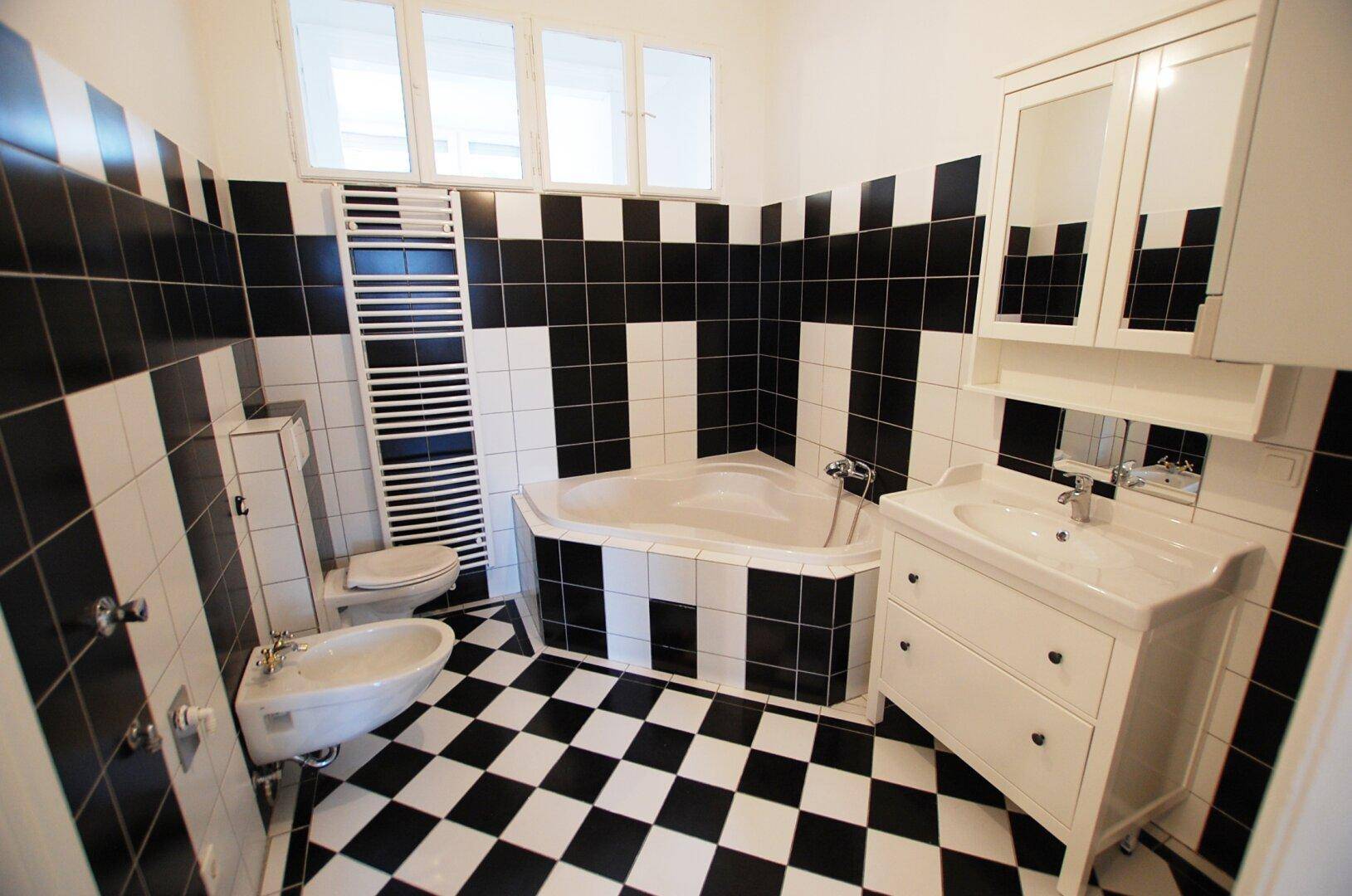 Geräumiges Badezimmer mit markanten schwarz-weißen Fliesen, Eckbadewanne und Bidet.