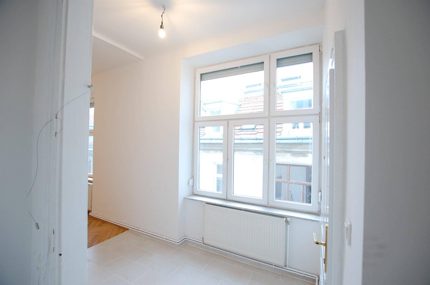 Lichtdurchfluteter Raum mit Fliesenboden und großem Fenster, ideal als Eingangsbereich.