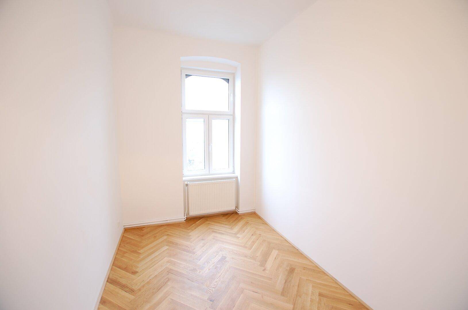 Kleiner, heller Raum mit Fischgrätparkett und einem Fenster, ideal als Schlaf- oder Arbeitszimmer.
