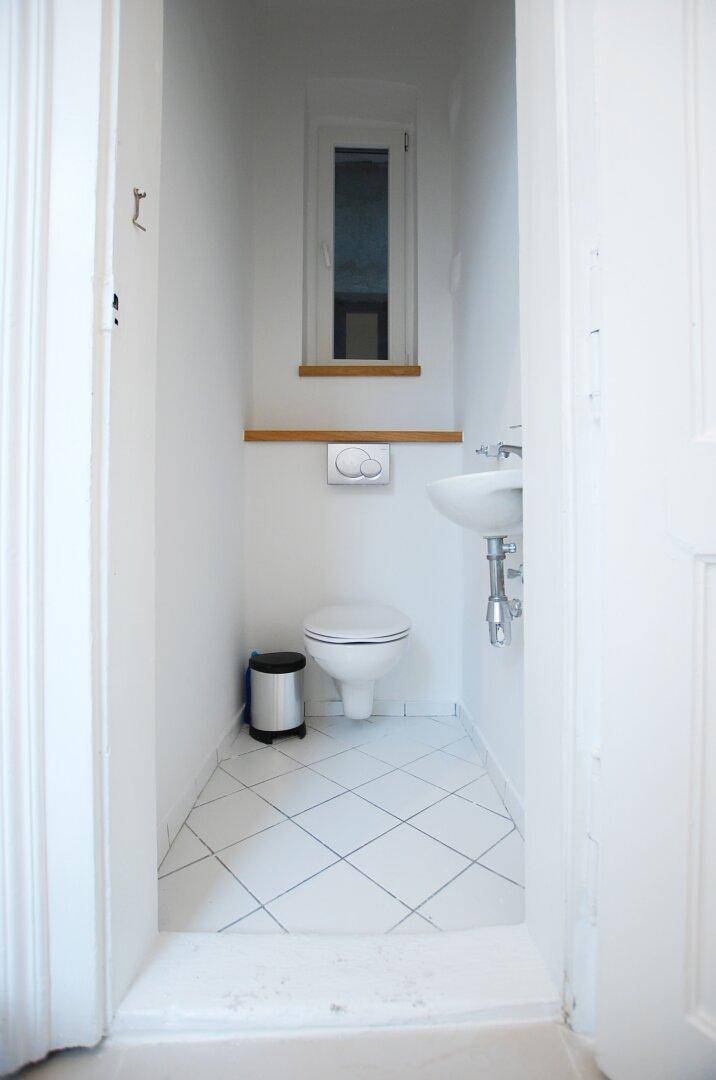 Kleines Gäste-WC mit weißen Fliesen, wandhängendem WC und schmalem Fenster.
