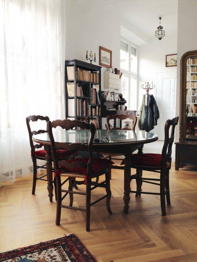 Gemütlicher Essbereich mit rundem Tisch, Holzstühlen und Bücherregal, auf Fischgrätparkett.