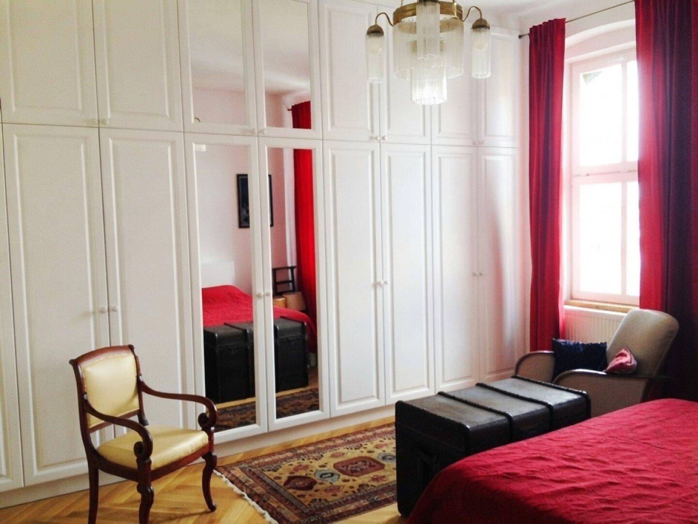 Schlafzimmer mit großen weißen Einbauschränken, Spiegeln und roten Vorhängen.