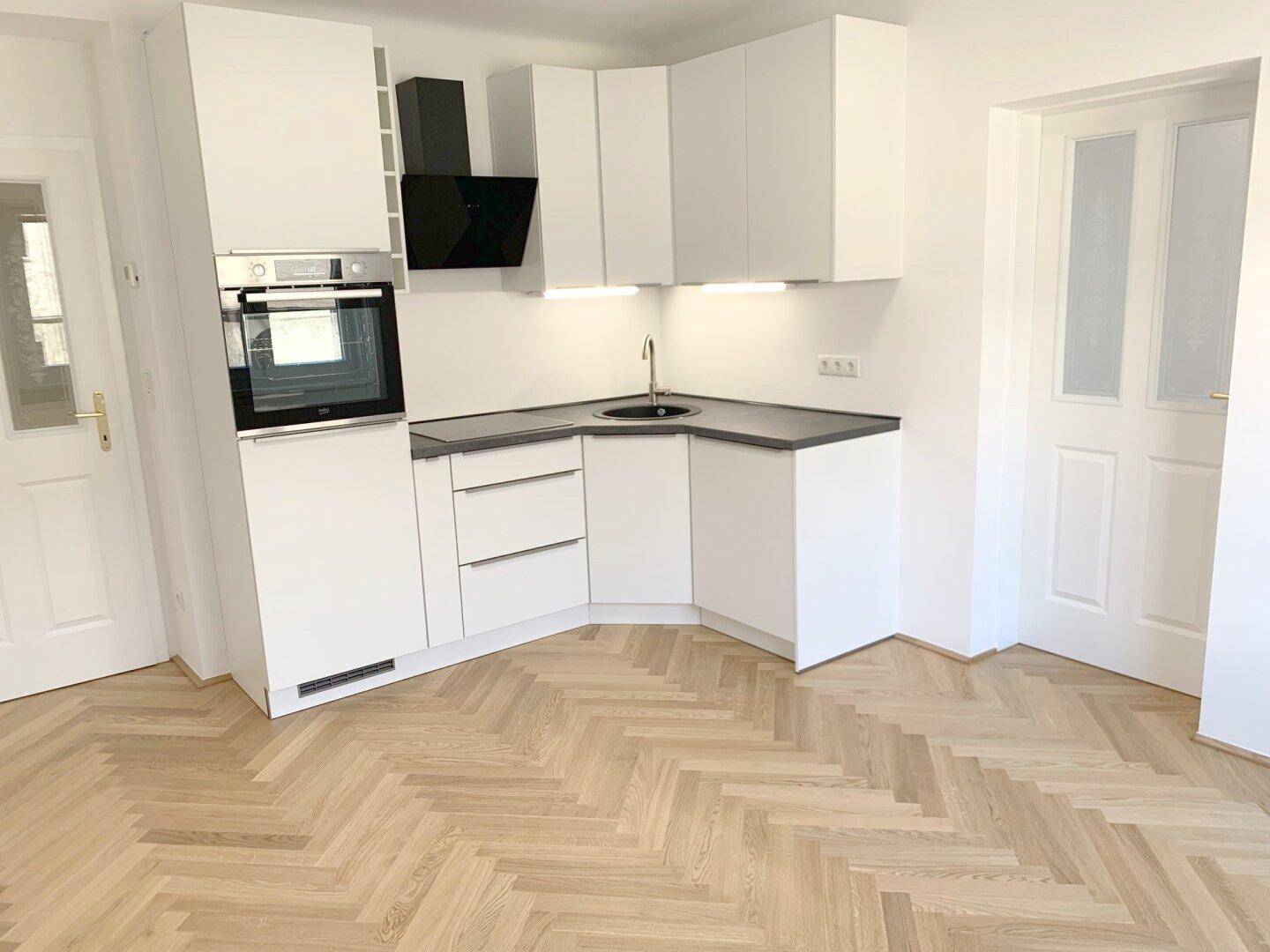 Moderne Einbauküche mit weißen Schränken, dunkler Arbeitsplatte und integriertem Backofen.