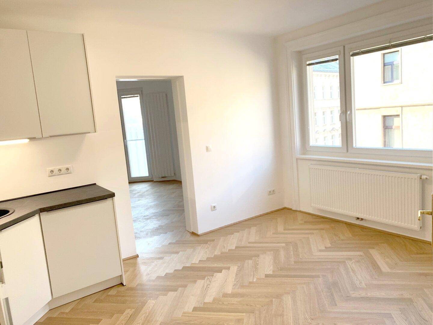 Offener Bereich mit moderner Küche und Zugang zu einem weiteren hellen Zimmer.