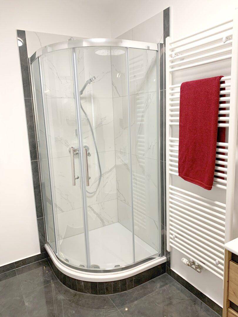 Moderne Duschkabine mit Glaswänden und Fliesen in Marmoroptik im Badezimmer.