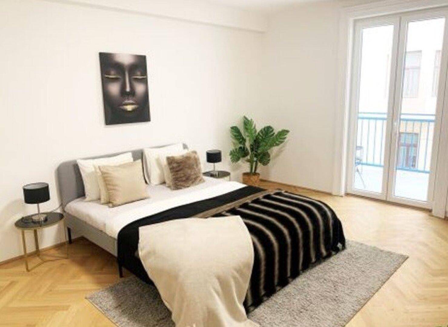 Helles Schlafzimmer mit Doppelbett, Fischgrätparkett und Zugang zu einem französischen Balkon.