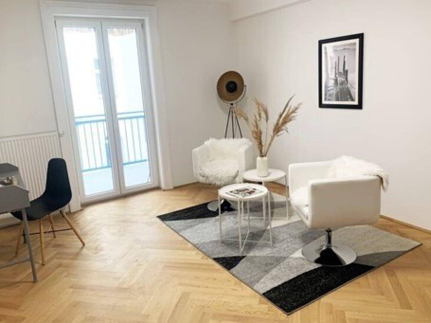 Heller Wohnbereich mit modernen Sesseln, Teppich und Zugang zu einem französischen Balkon.