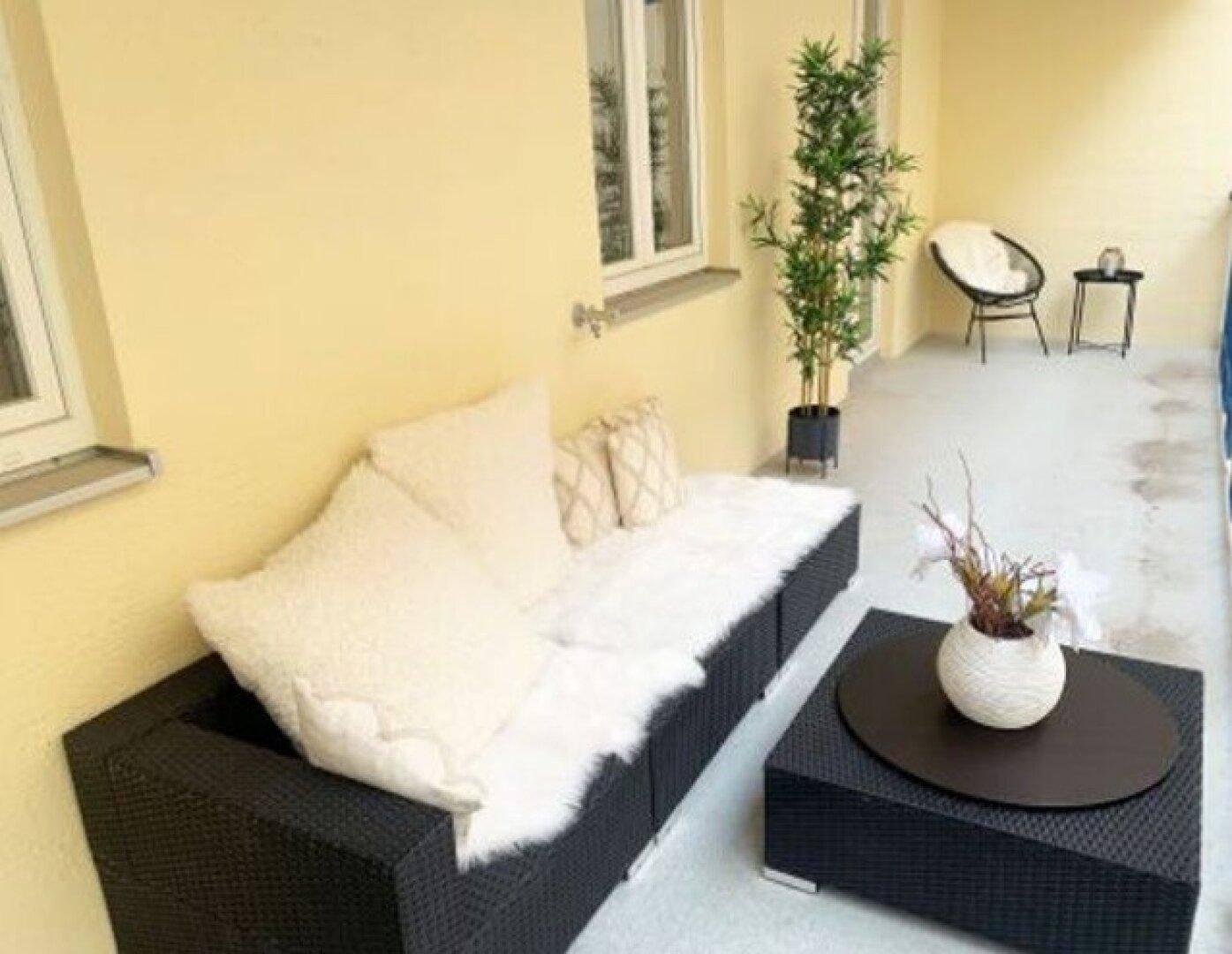 Gemütlicher Außenbereich auf dem Balkon mit Rattanmöbeln und Pflanzen für entspannte Stunden.