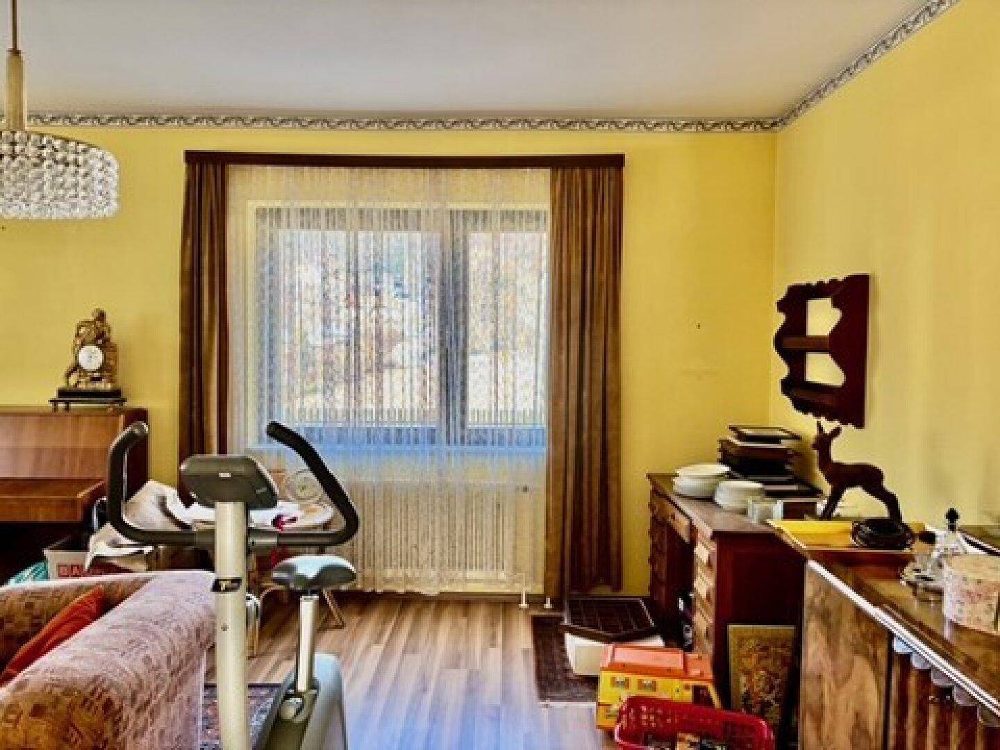 Gemütliches Wohnzimmer mit gelben Wänden, Holzfußboden und einem großen Fenster, hell und einladend.