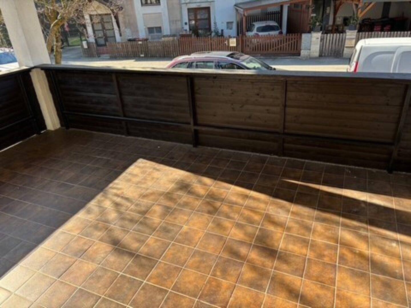 Geflieste Terrasse mit dunklem Holzgeländer und Blick auf die Straße, sonnig und offen.