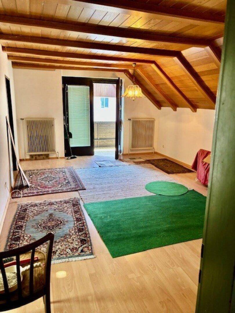 Dachgeschosszimmer mit sichtbaren Holzbalken, Holzfußboden und Zugang zu einem Außenbereich.