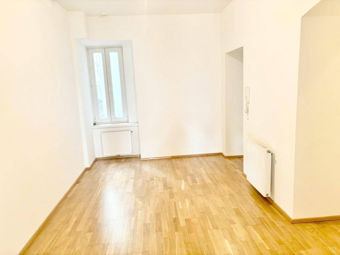 Kleinerer, heller Raum mit Holzparkettboden, einem Fenster und weiß gestrichenen Wänden.