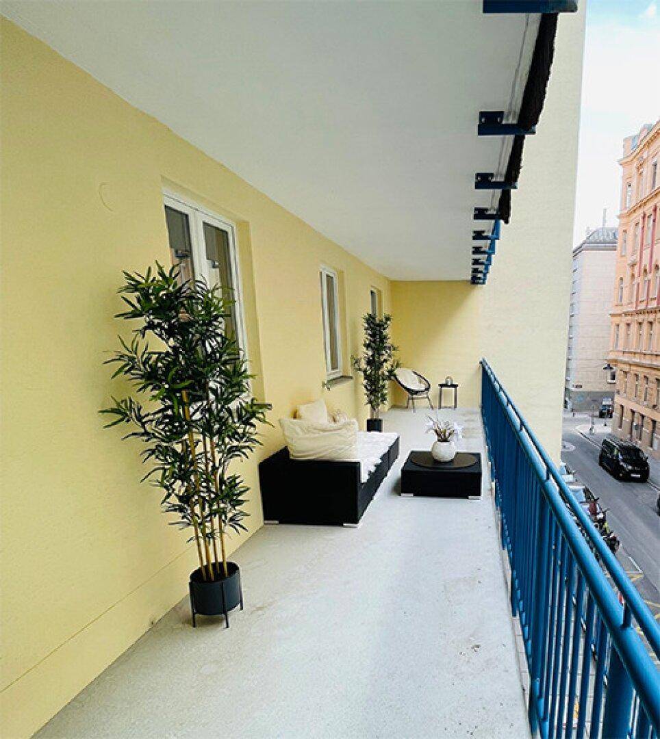 Langer Balkon mit Sitzgelegenheiten und Blick auf die Straße, ideal für entspannte Momente.