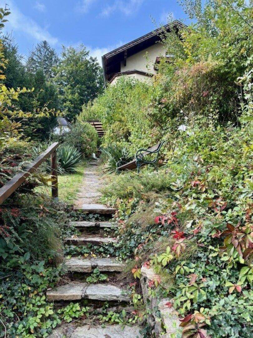 Steinerner Gartenweg führt einen bewachsenen Hang hinauf zu einem versteckten Sitzbereich.