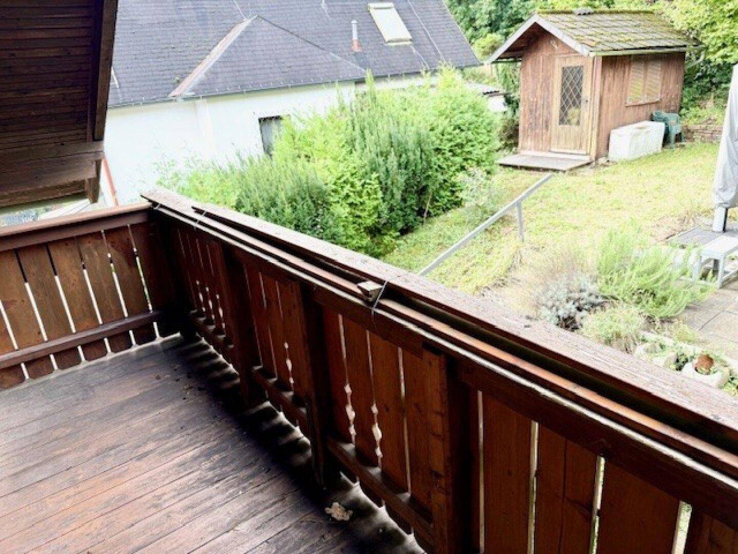 Rustikaler Holzbalkon mit Blick auf den grünen Garten und die umliegende Natur.