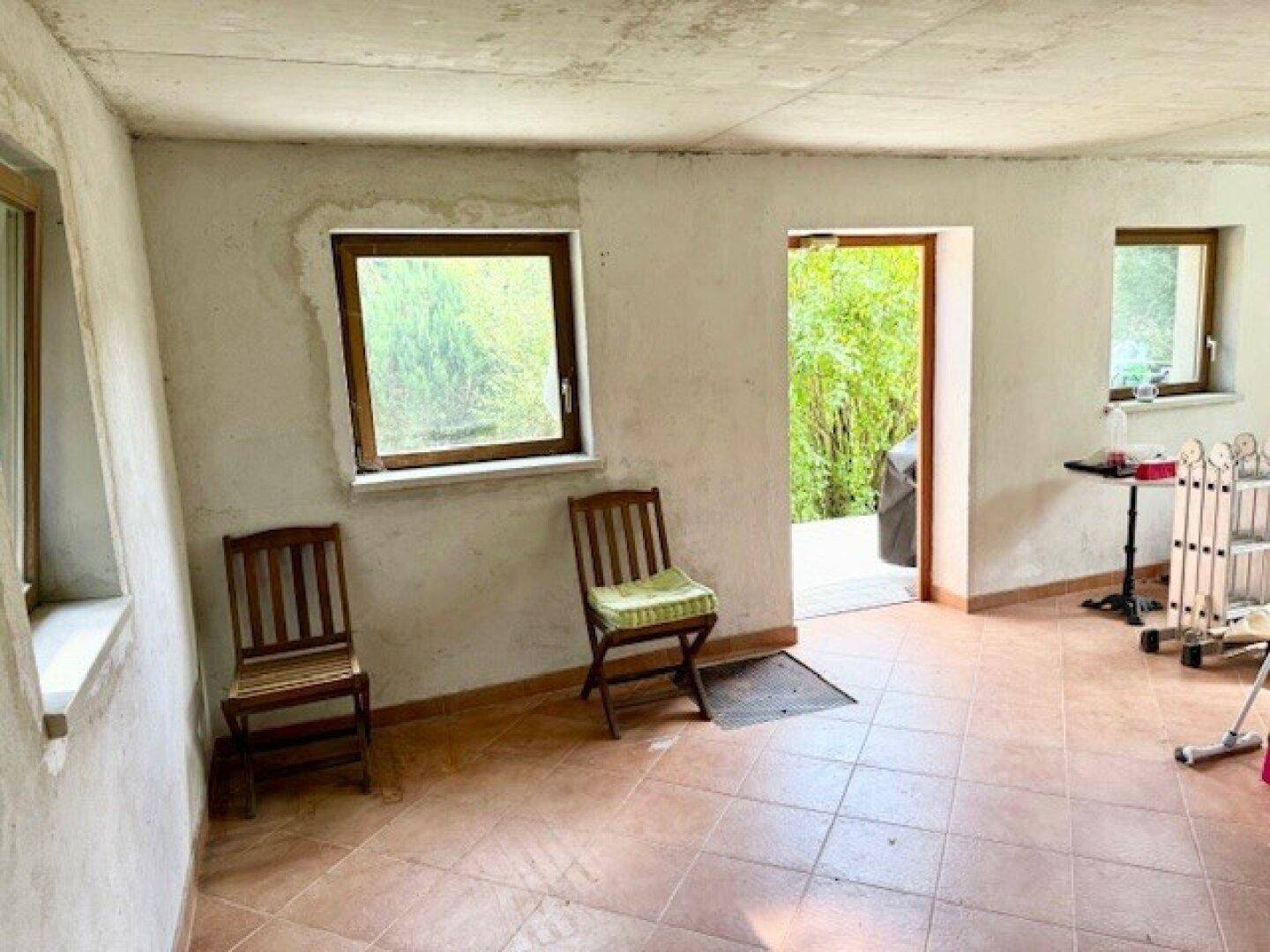 Unfertiger Raum mit Fliesenboden, Fenstern und Zugang zum Außenbereich, bereit für die Gestaltung.