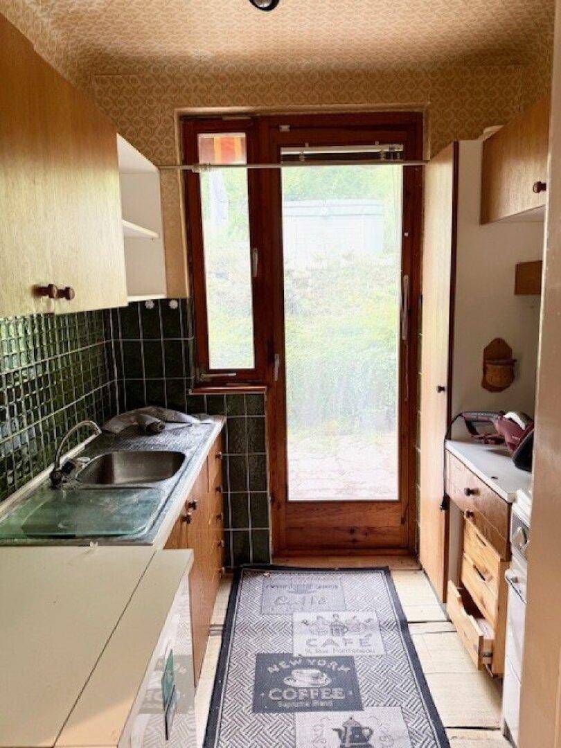 Kleine Küche mit Holzschränken, grünen Fliesen und direktem Zugang zum Garten.
