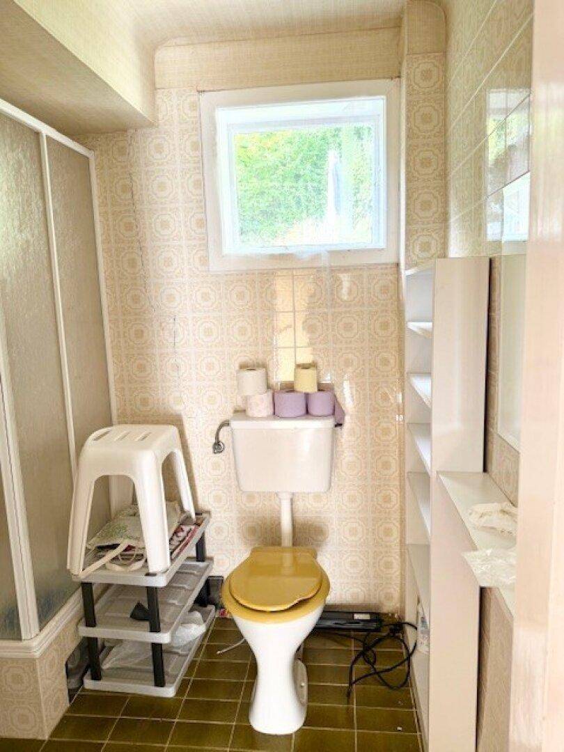 Badezimmer mit Toilette, Fenster und gemusterten Wandfliesen in hellem Design.