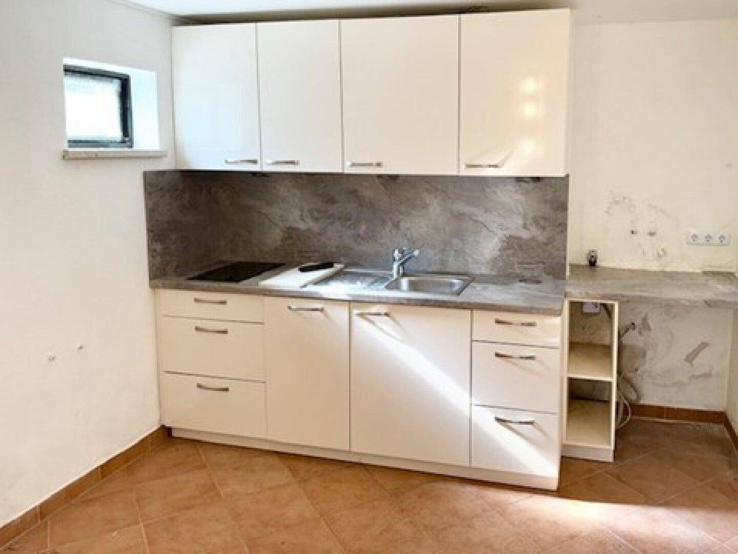 Moderne Küchenzeile mit weißen Schränken, Induktionskochfeld und grauer Arbeitsplatte.