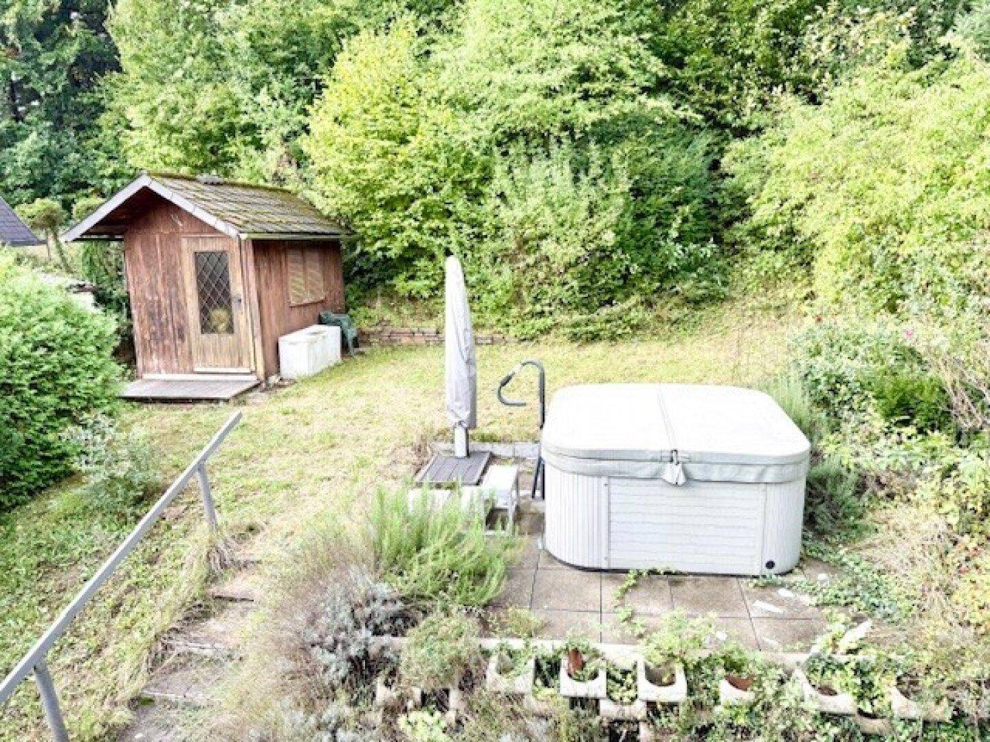 Gepflegter Gartenbereich mit Whirlpool, Gartenhaus und üppiger Vegetation.