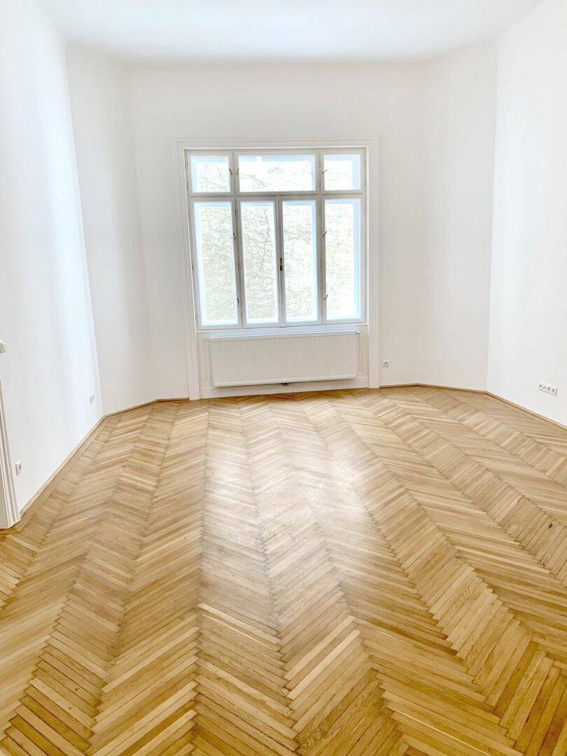 Heller Raum mit Fischgrätparkett und großem Fenster, ideal als Wohn- oder Schlafzimmer.
