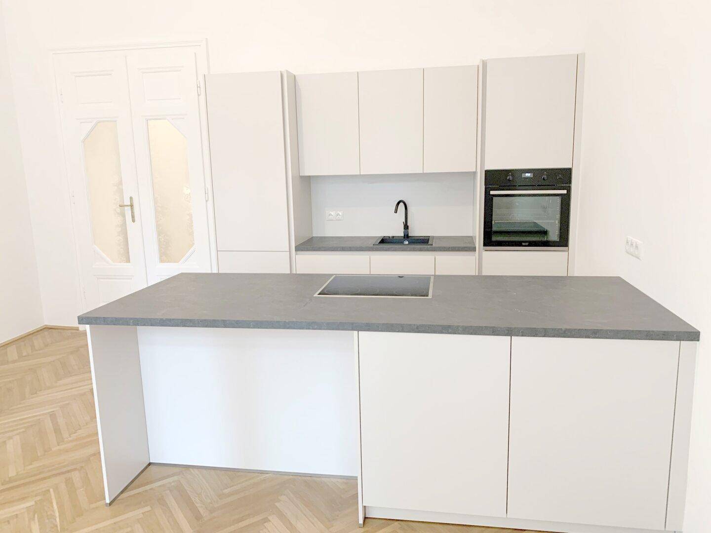 Moderne Einbauküche mit weißen Schränken, grauer Arbeitsplatte und Kochinsel mit Induktionskochfeld.