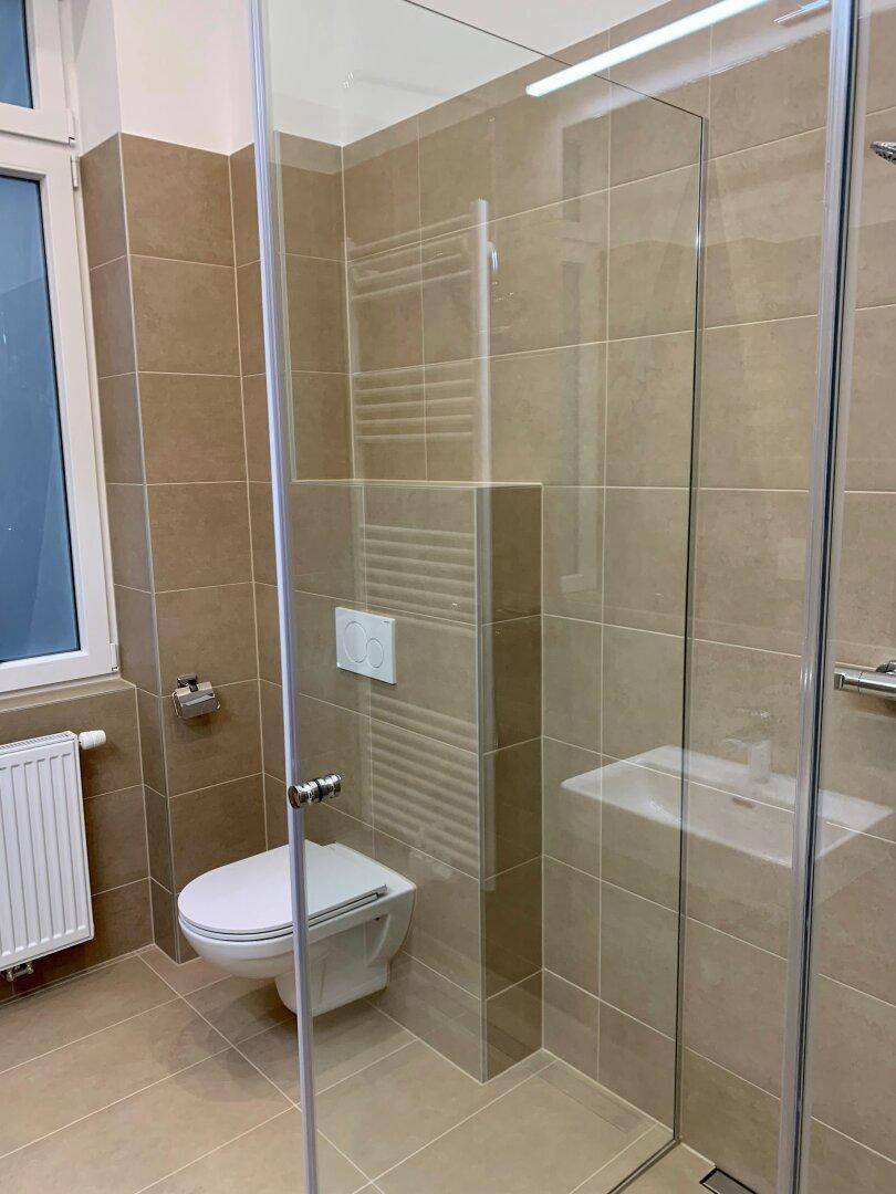 Modernes Badezimmer mit beigefarbenen Fliesen, wandhängendem WC und Glasdusche.