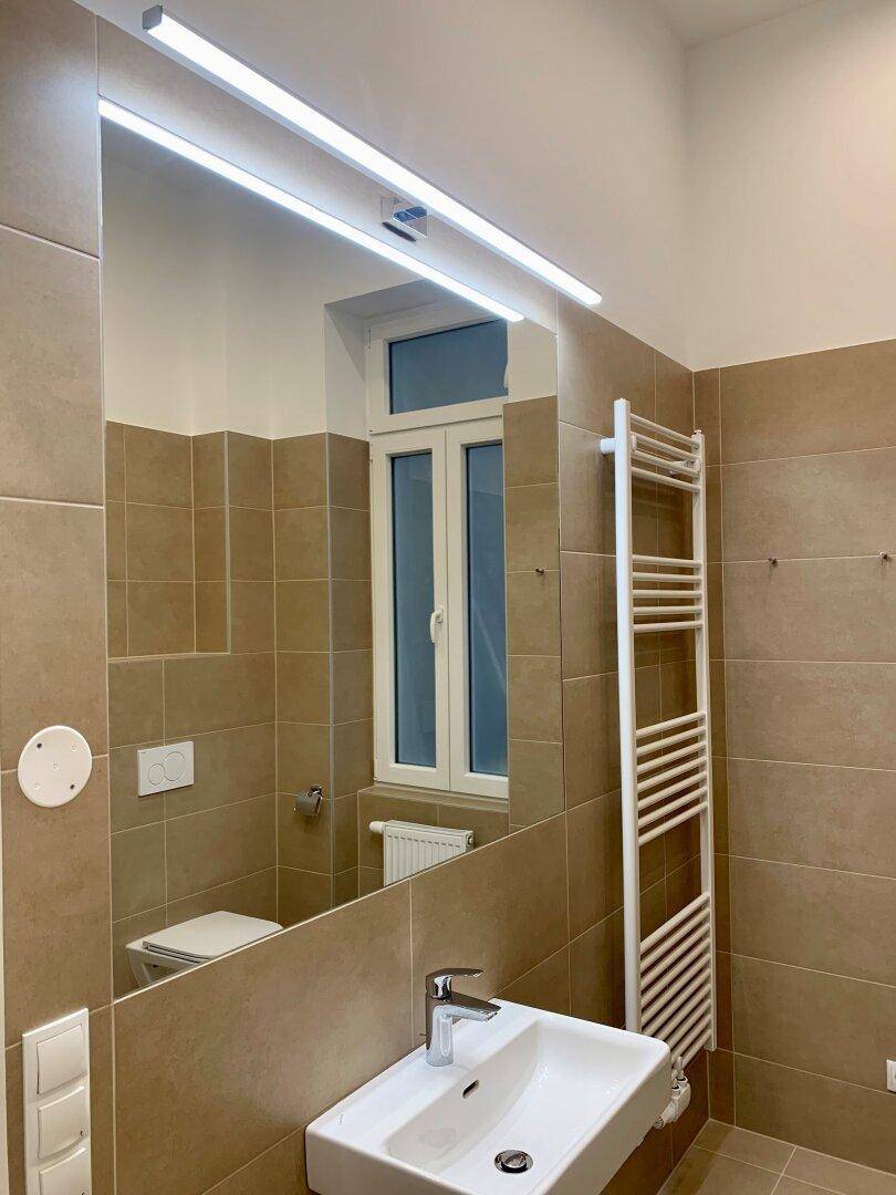 Badezimmer mit modernem Waschtisch, großem Spiegel und beheiztem Handtuchhalter.