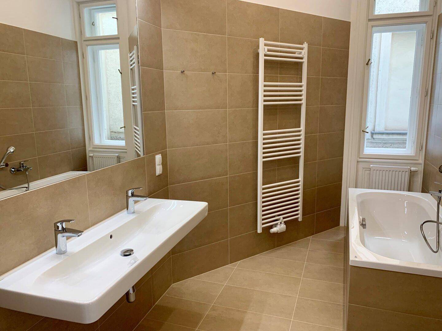 Geräumiges Badezimmer mit Doppelwaschbecken, Badewanne und beheiztem Handtuchhalter.