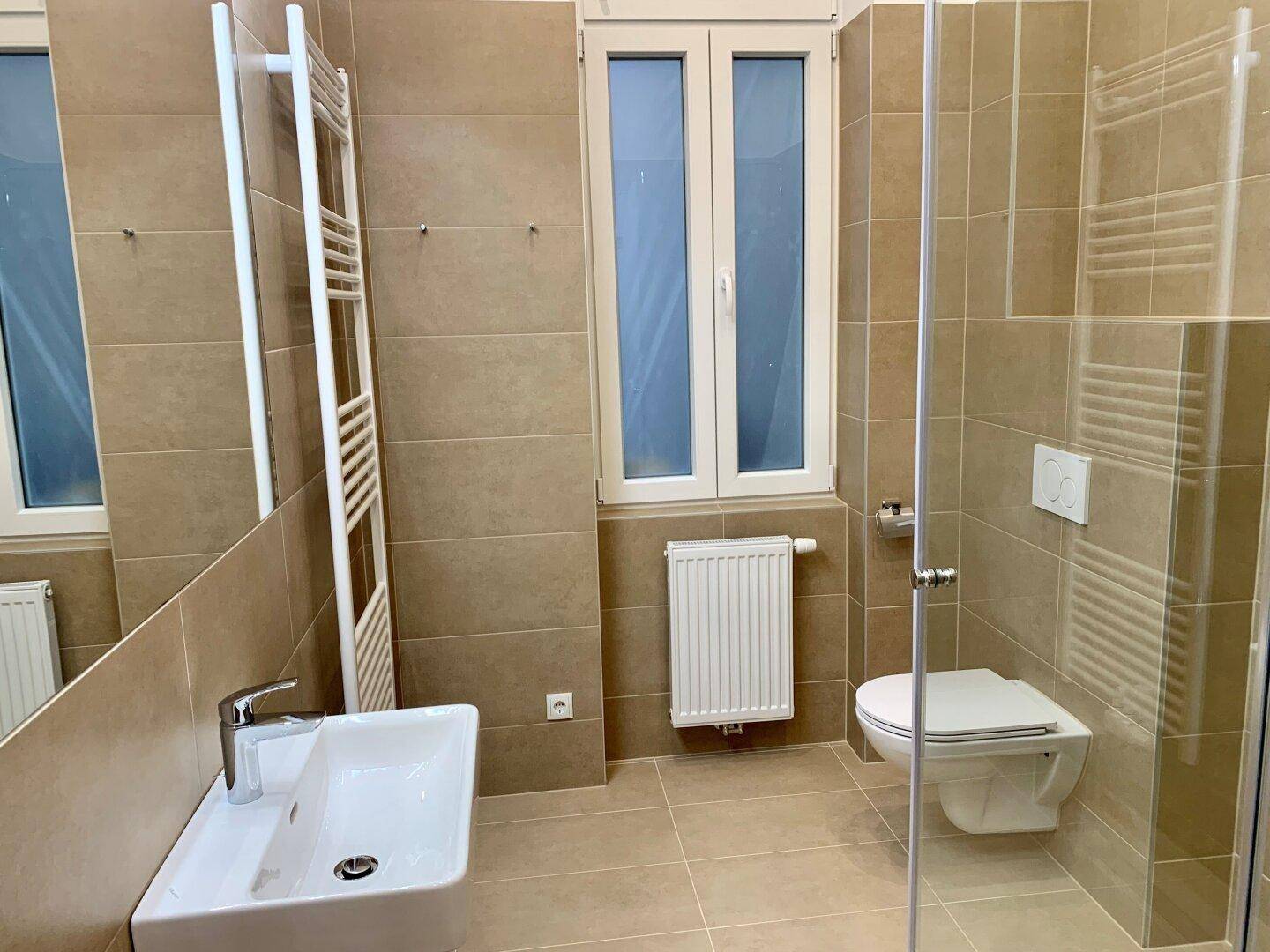 Helles Badezimmer mit Waschtisch, wandhängendem WC, Dusche und Fenster.