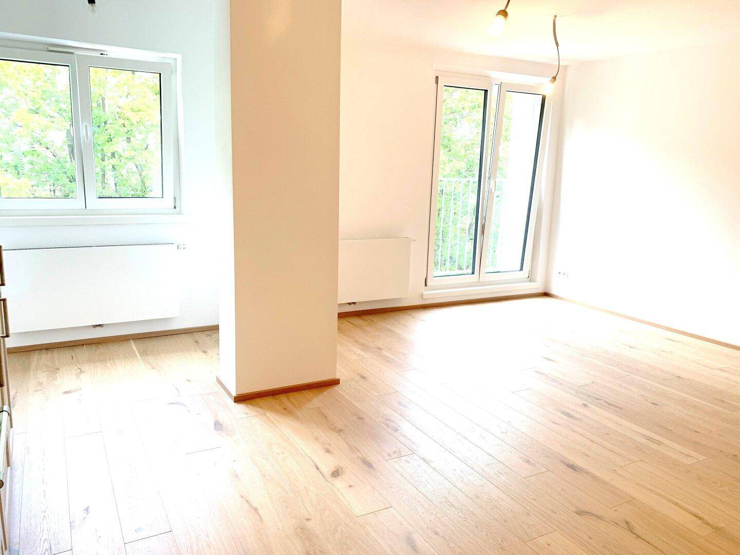Lichtdurchfluteter Wohnbereich mit Holzboden und mehreren Fenstern, die viel Tageslicht bieten.