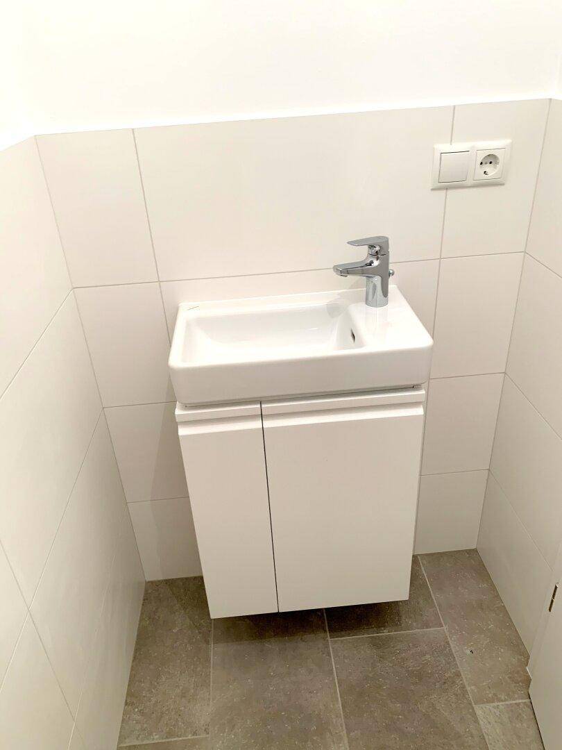 Kleines Gäste-WC mit modernem Waschtisch und hellen Fliesen.