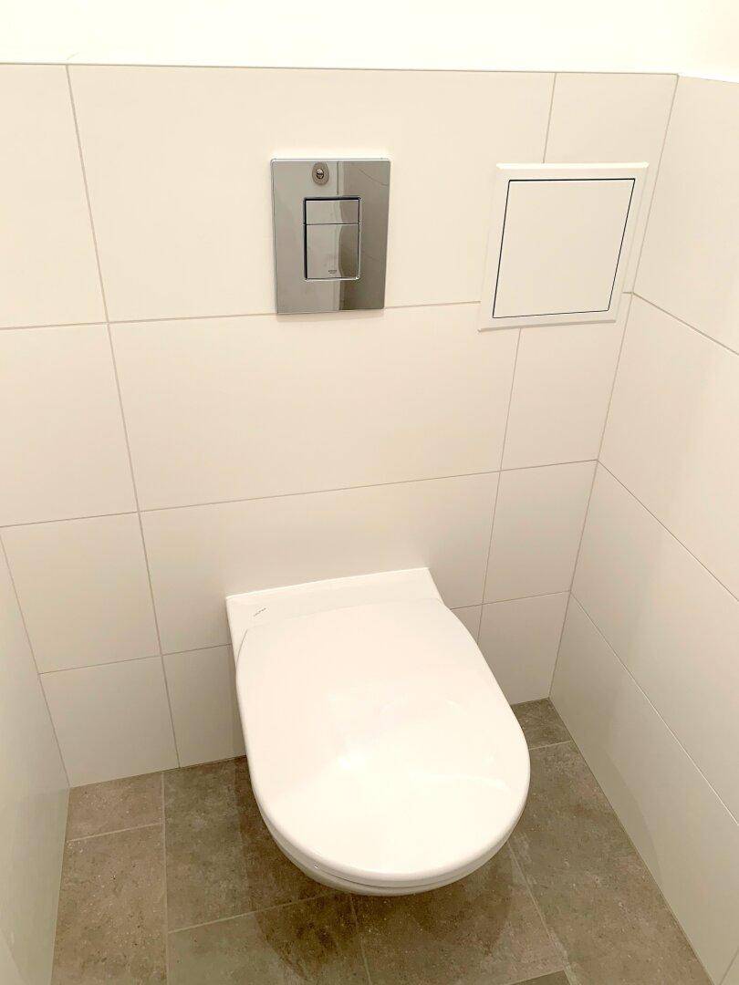 Modernes Wand-WC mit Spülkasten und hellen Fliesen im Gäste-WC.