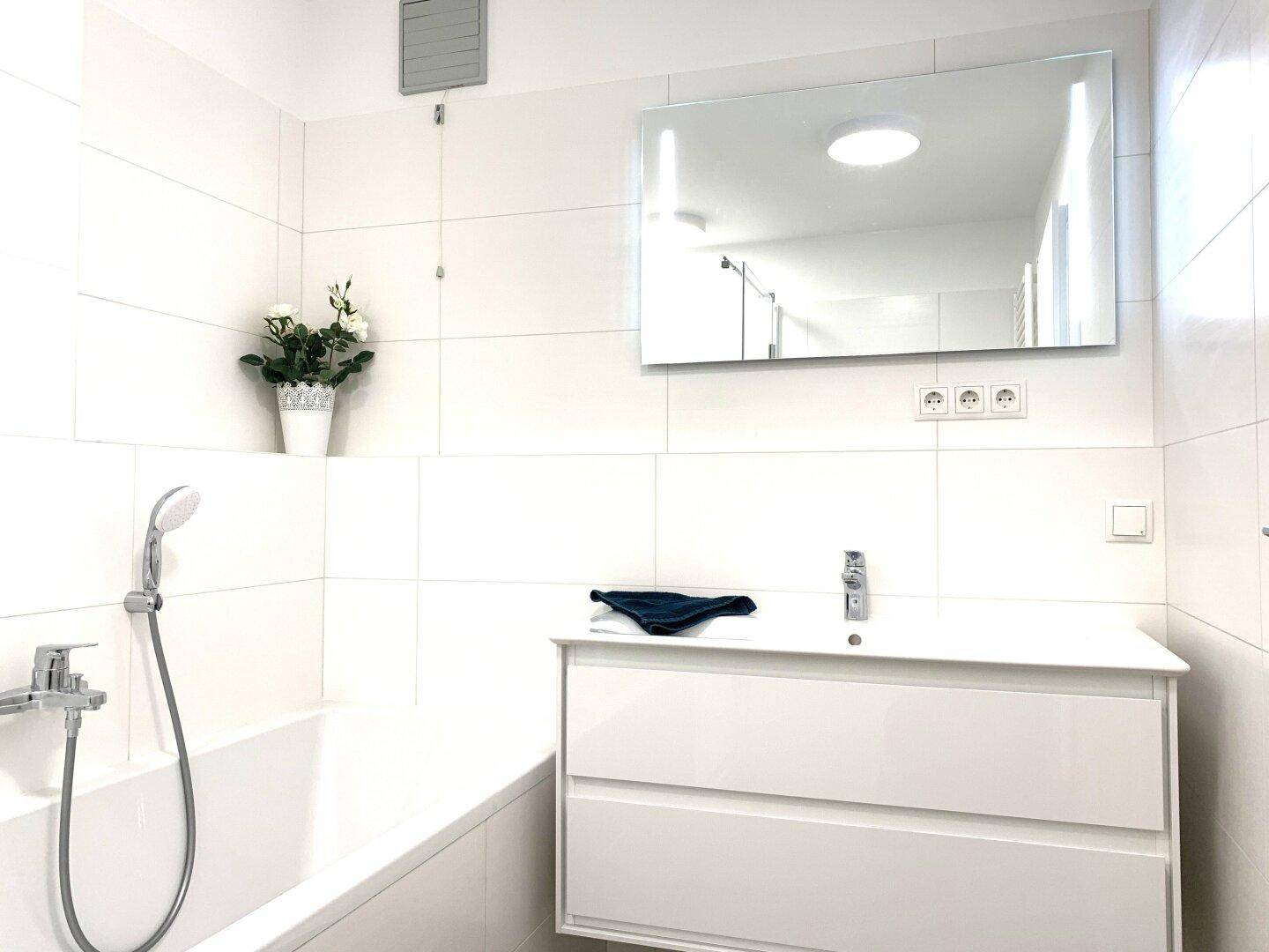Helles Badezimmer mit modernem Waschtisch, Badewanne und beleuchtetem Spiegel.