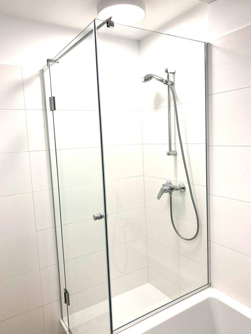 Moderne Dusche mit Glasabtrennung und Handbrause in einem hell gefliesten Bad.
