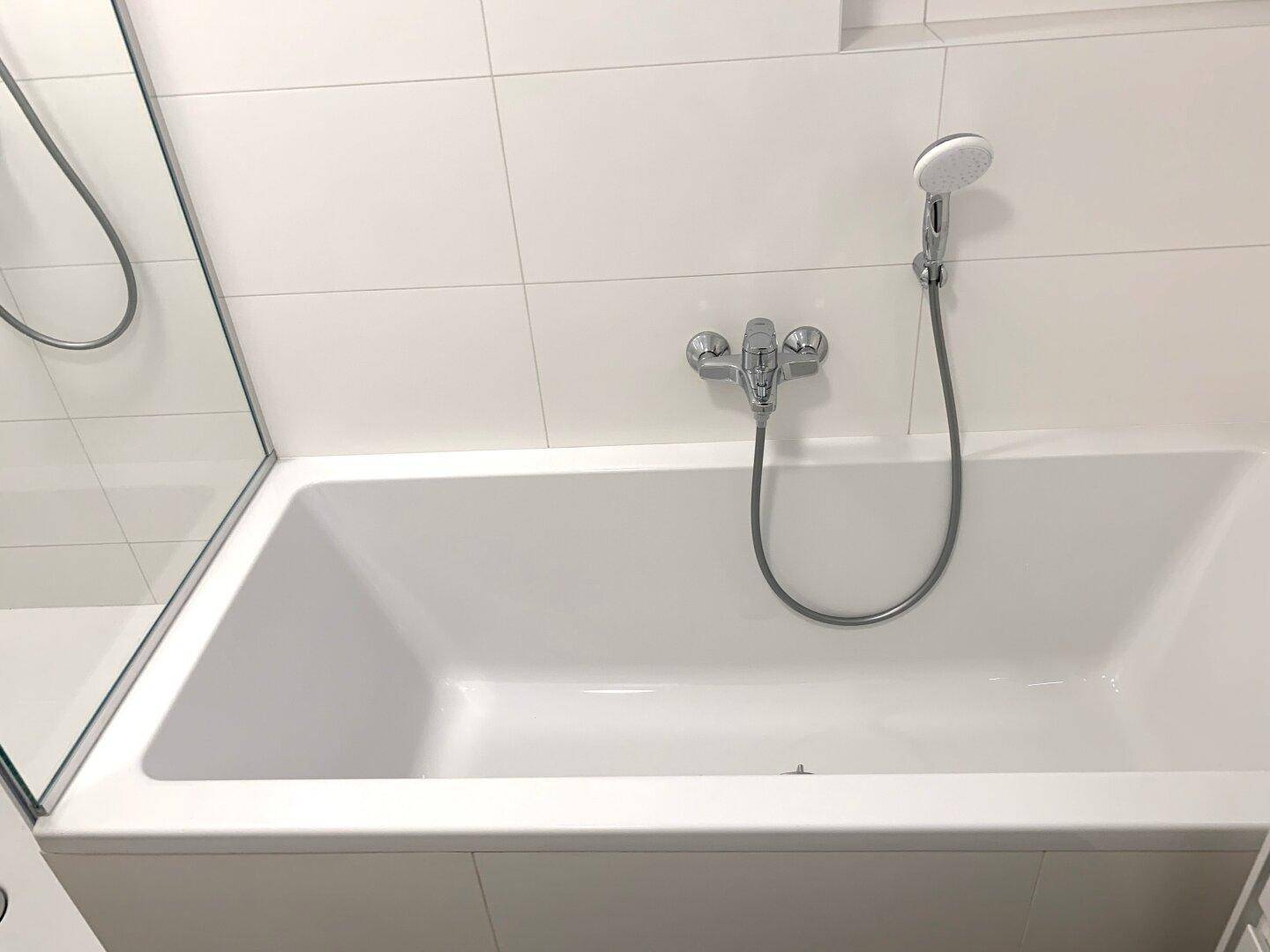 Saubere, moderne Badewanne mit Handbrause in einem hellen Badezimmer.
