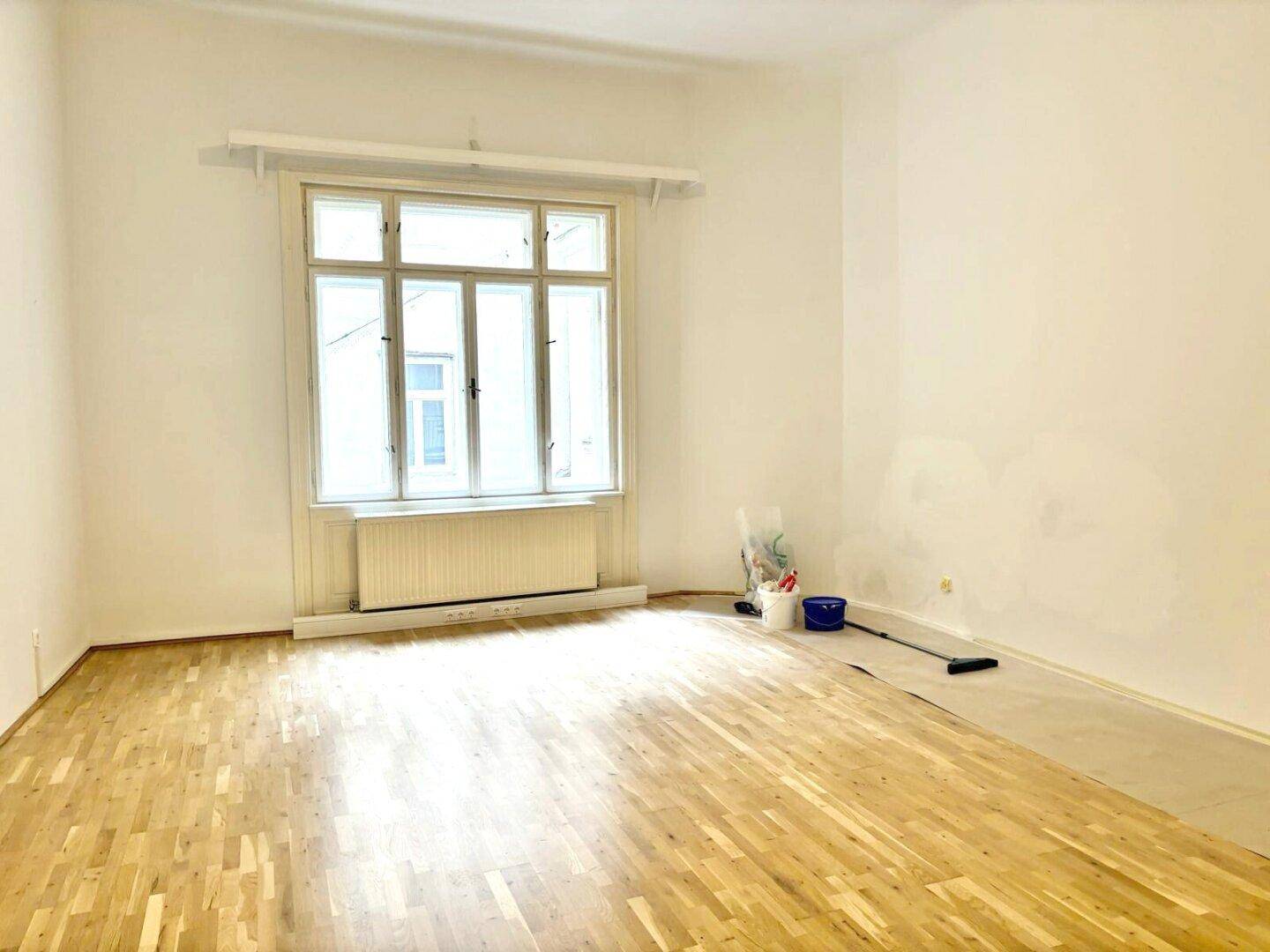 Geräumiges Zimmer mit Holzboden und großem Fenster, bereit für die Renovierung.