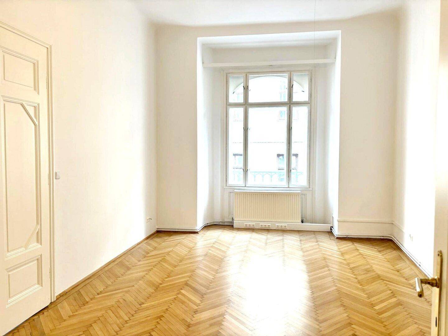Lichtdurchflutetes Zimmer mit Fischgrätparkett, weißen Wänden und einem Erkerfenster.