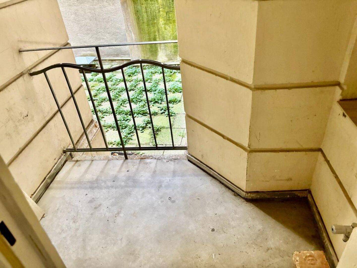 Kleine Loggia mit Blick auf einen begrünten Innenhof und schmiedeeisernem Geländer.