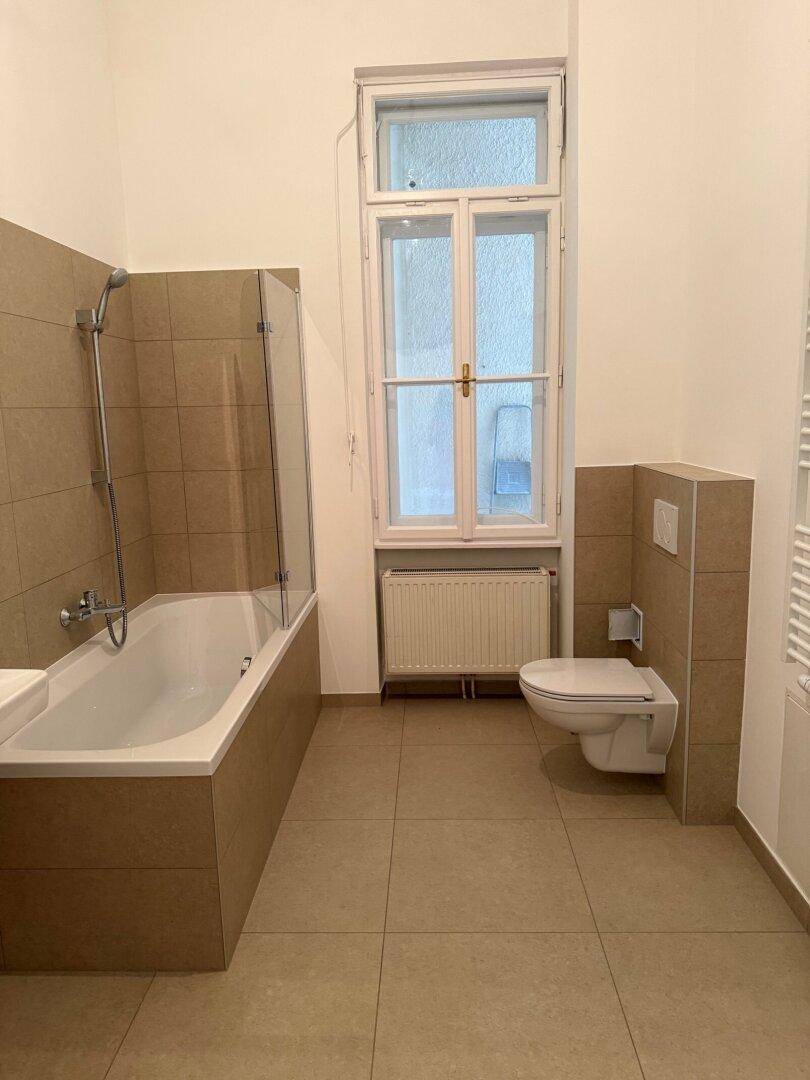 Modernes Badezimmer mit Badewanne, Dusche und wandhängendem WC, hell gefliest.