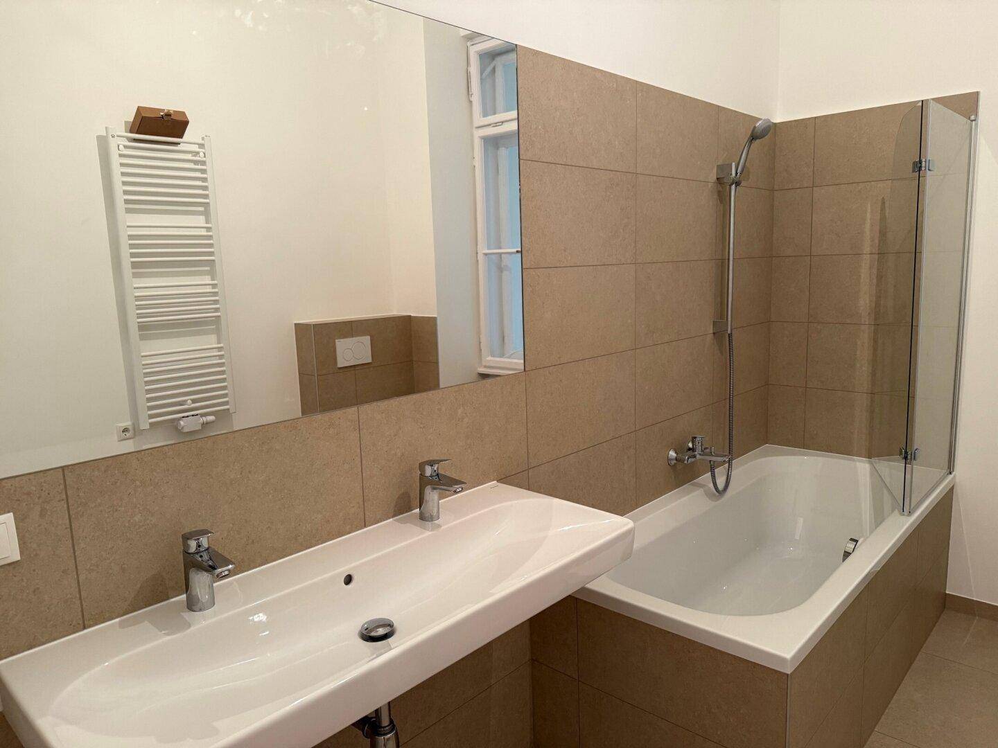 Badezimmer mit Doppelwaschbecken, Badewanne mit Duschabtrennung und großem Spiegel.