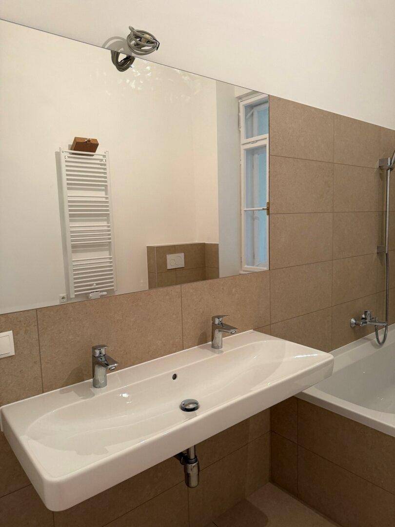 Modernes Badezimmer mit Doppelwaschbecken, Badewanne mit Duschabtrennung und großem Spiegel.