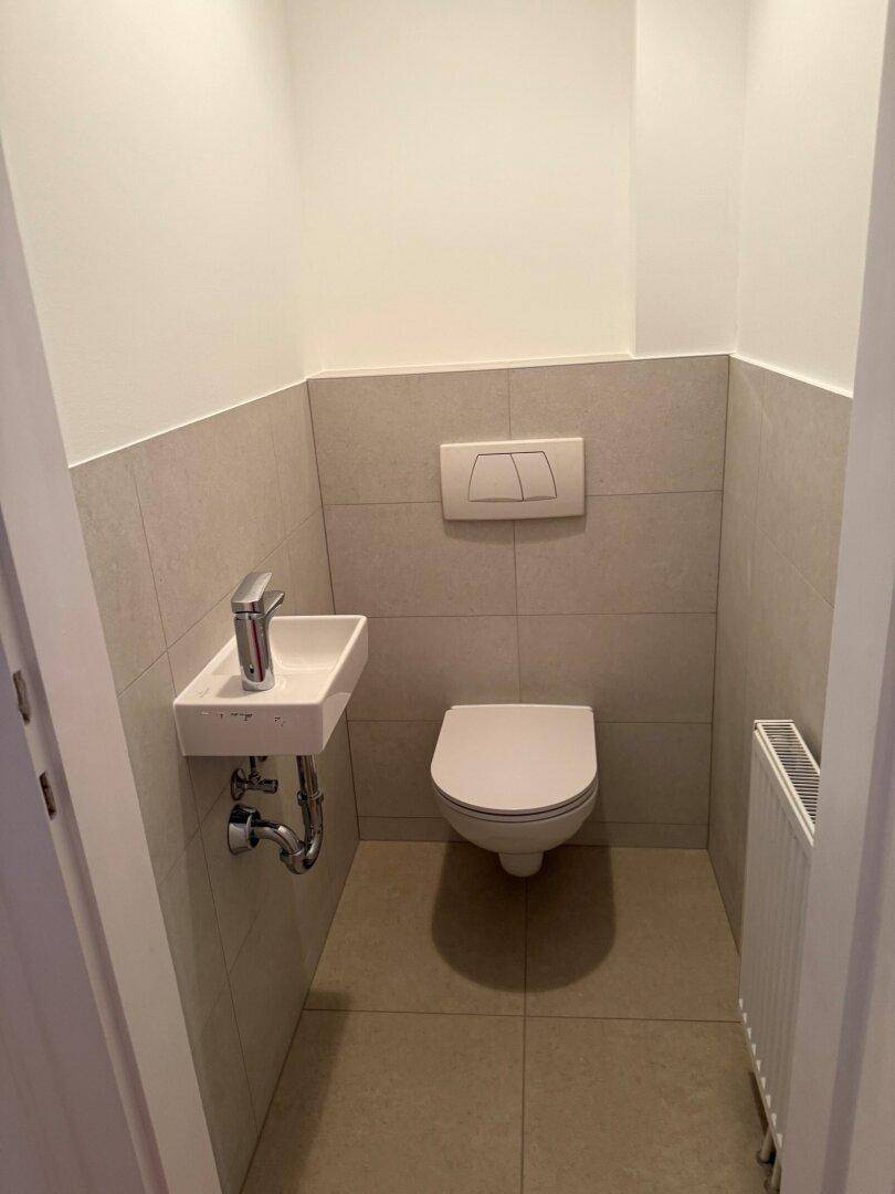 Kleines Gäste-WC mit wandhängender Toilette und kompaktem Waschbecken, hell gefliest.